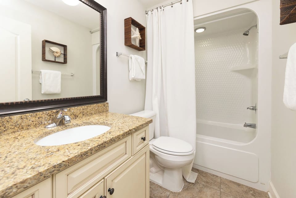This guest bath features a stylish granite countertop, elegant mirror, and coastal decor, creating a refreshing atmosphere