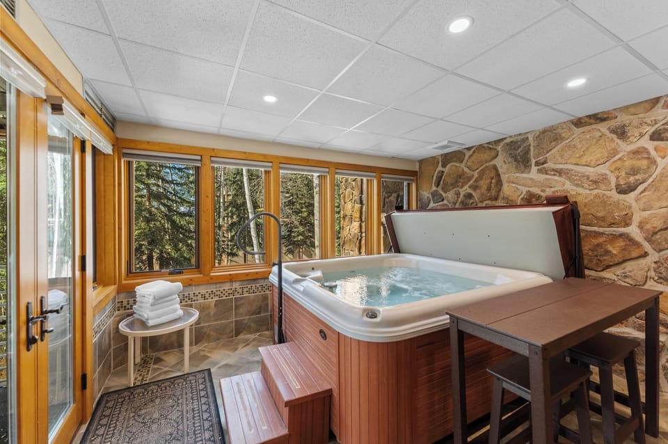 Unwind in your private hot tub surrounded by natural stone and panoramic forest views through floor-to-ceiling windows.
