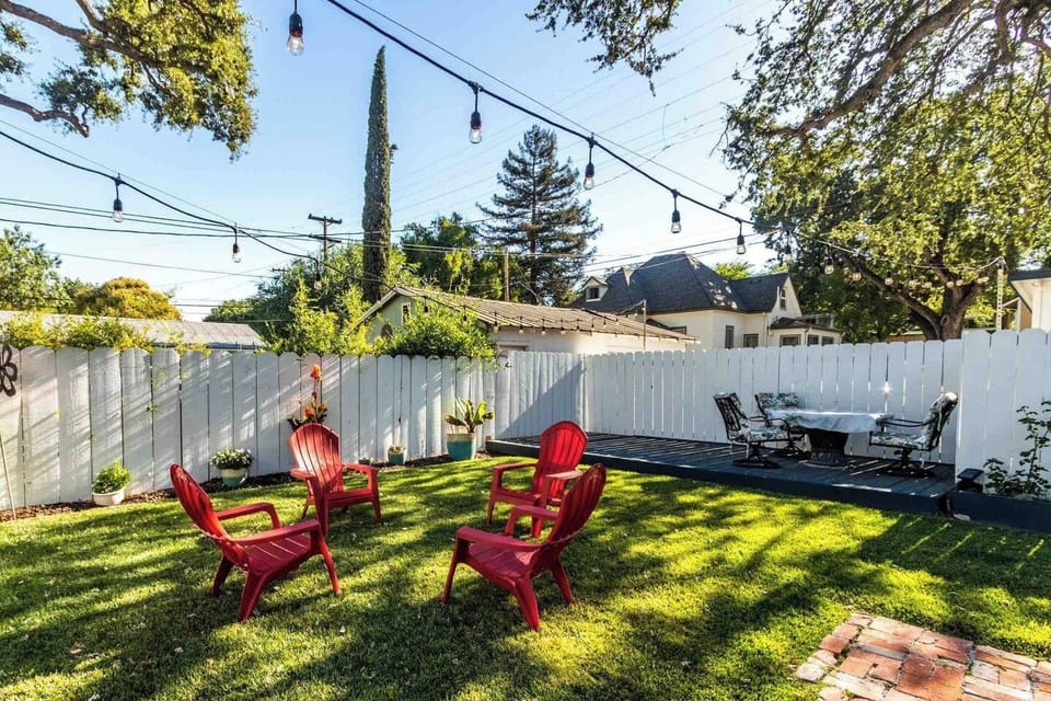 Spacious fenced backyard with Adirondack seating, string lights, and an outdoor dining area.