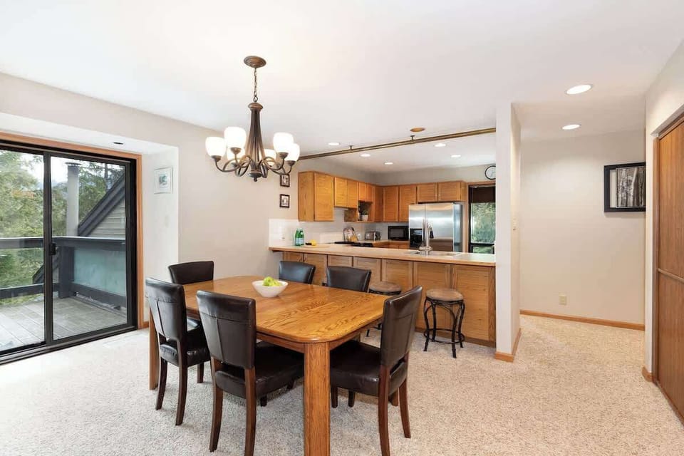 - Open dining area beside bright kitchen space  
- Wooden table setup for shared meals and laughter  
- Forest-view patio doors bring natural light inside  
