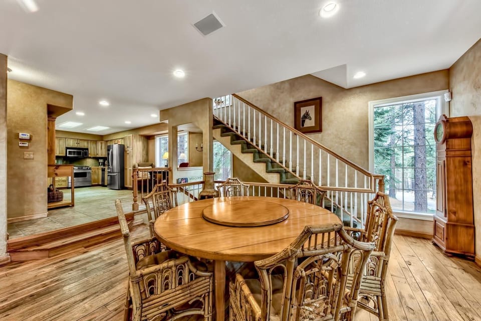 Your spacious dining room flows seamlessly into the kitchen, perfect for gathering around the beautiful wooden table with forest views streaming through large windows.
