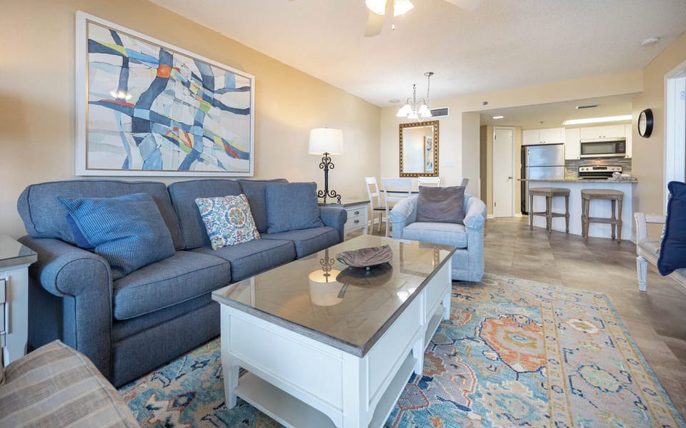Living area features a blue sofa with queen sleeper, a glass-top coffee table, and a dining space
