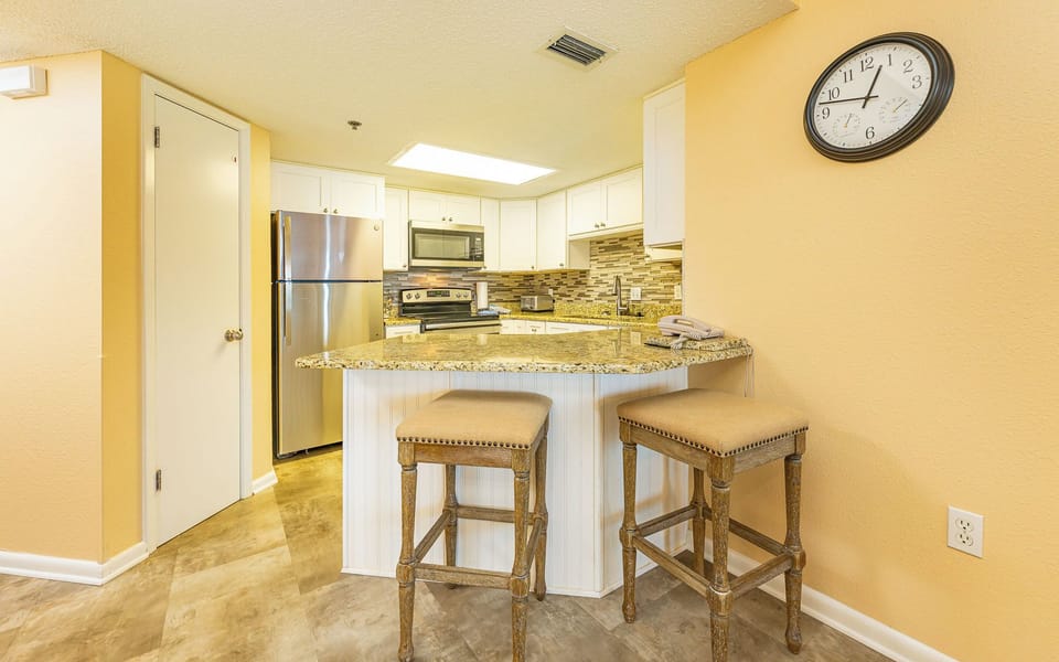 Bright kitchen area features granite countertops, stainless appliances, and a breakfast bar with two stylish stools