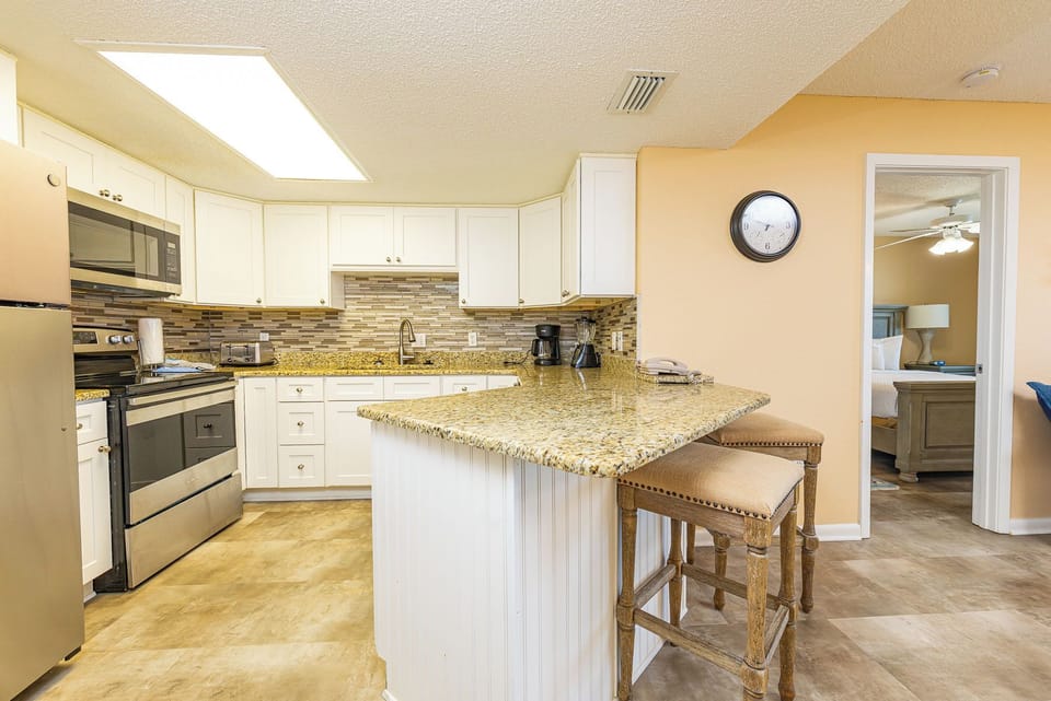 Kitchen features sleek cabinetry, a granite countertop breakfast bar with seating, and a view into the master suite