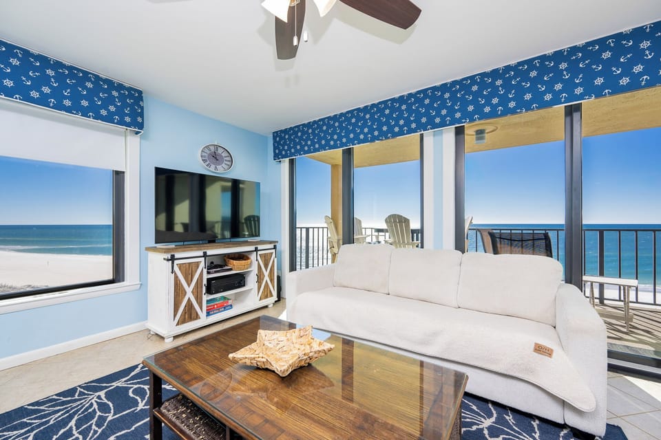 This inviting living area features a plush white sofa, a large TV, and breathtaking views of the beach from expansive windows