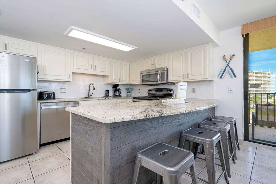 Bright kitchen features granite countertops, stainless appliances, and a breakfast bar with metal stools, perfect for dining