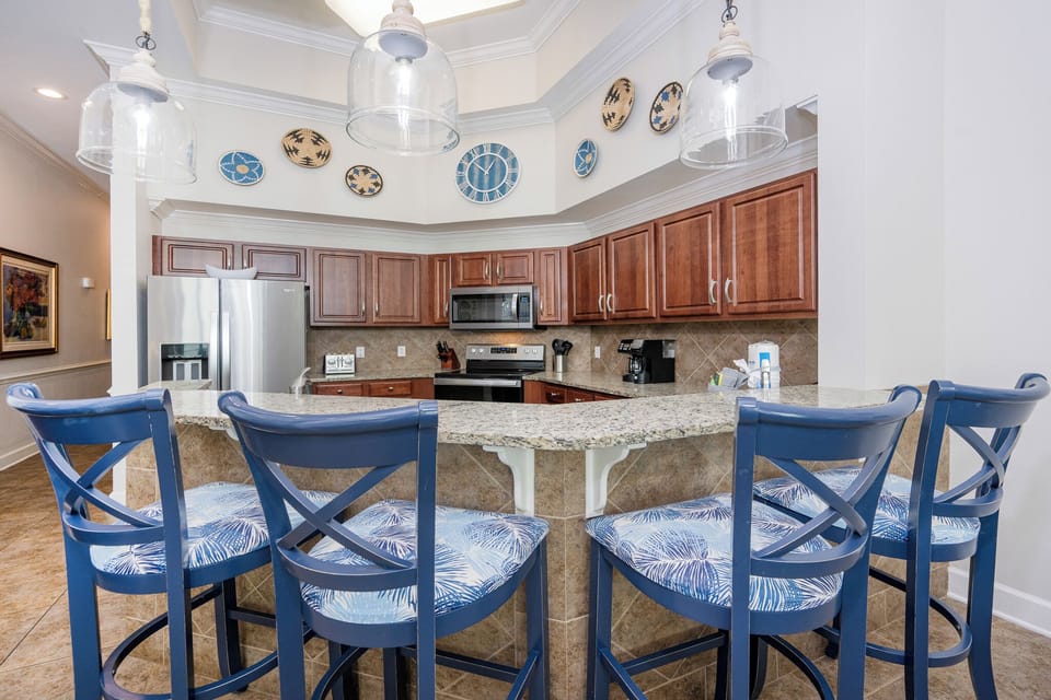 Kitchen featuring stainless appliances, granite countertops, and stylish bar seating with tropical-patterned cushions