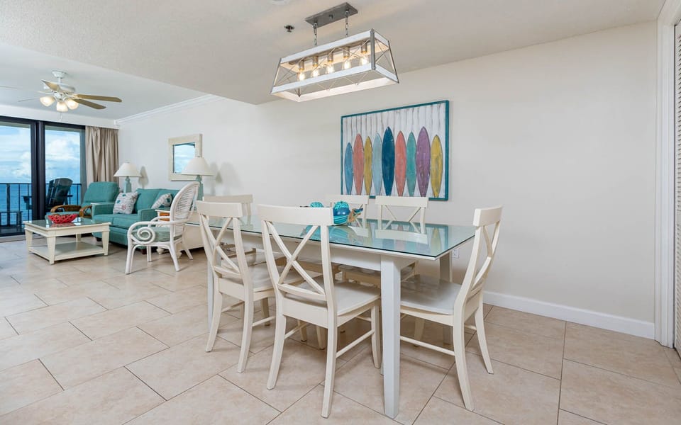 This inviting living area features a turquoise sofa with queen sleeper, a glass dining table, and vibrant surfboard art