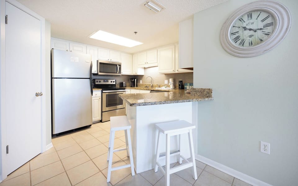 Bright kitchen featuring white cabinetry, granite countertops, and a breakfast bar with two stools for casual dining