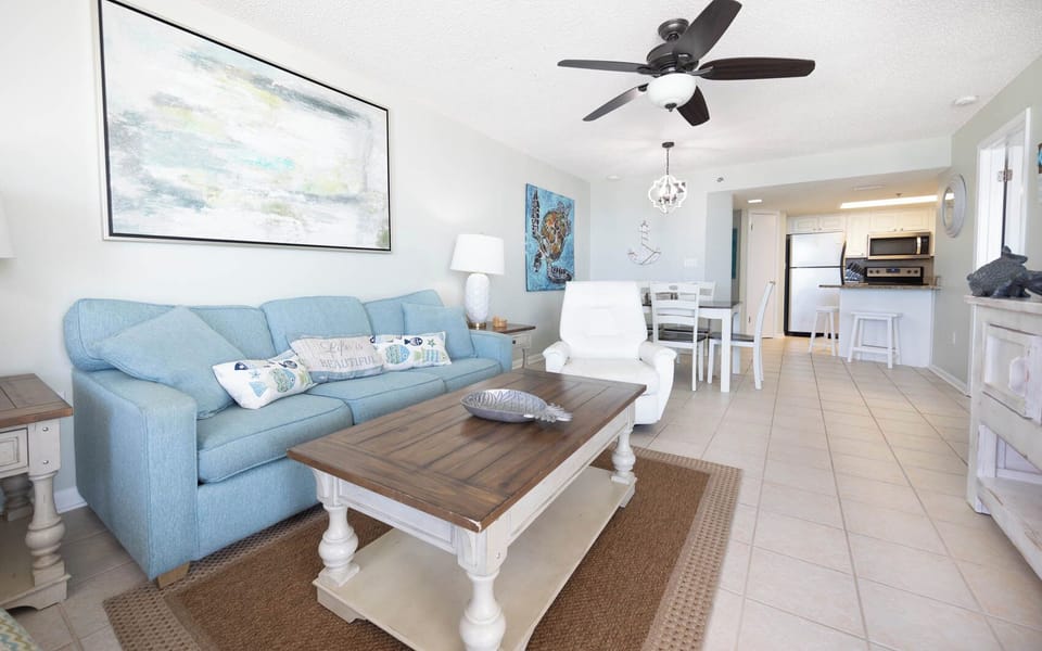 The inviting living area features a light blue sofa with a queen sleeper, a wooden coffee table, and a dining space nearby