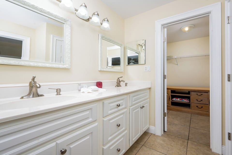 The master bathroom features elegant white cabinetry, dual mirrors, and a spacious closet for added convenience