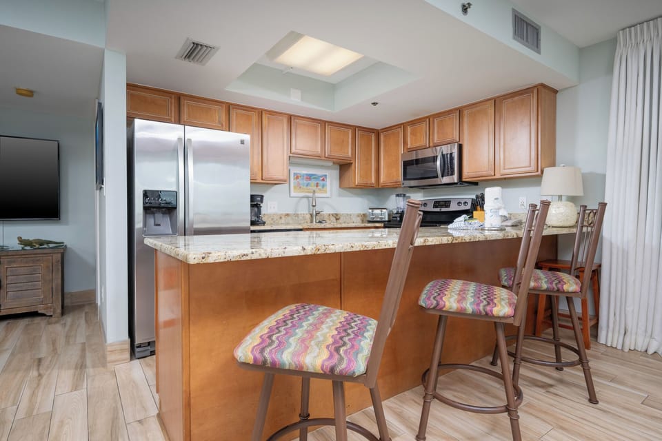 Kitchen featuring stainless appliances, granite countertops, and colorful bar stools for casual dining
