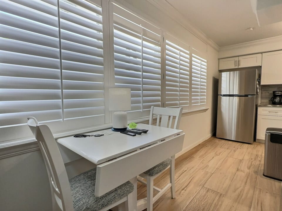 Dining area with table, chairs, plantation shutters, and view to kitchen with stainless refrigerator