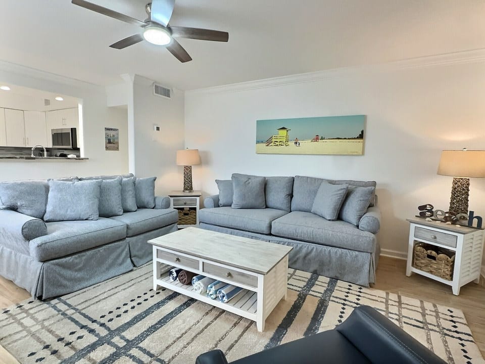 Living room with sofa, coffee table, ceiling fan, and beach wall art