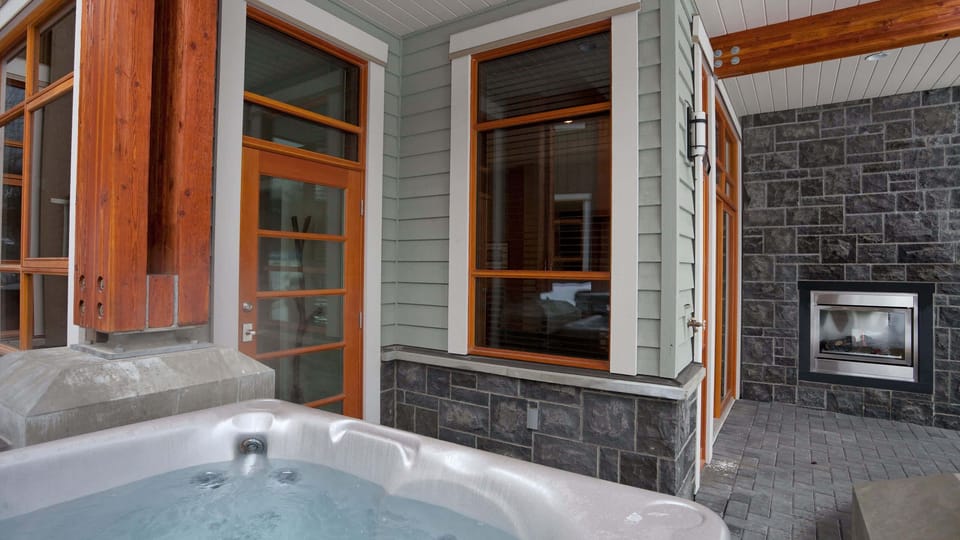 - Private outdoor hot tub beside a stone fireplace for ultimate mountain relaxation  
- Steam rises against cool alpine air creating the perfect après-ski unwind  
- Enjoy fireside warmth and bubbling comfort under the crisp mountain sky  