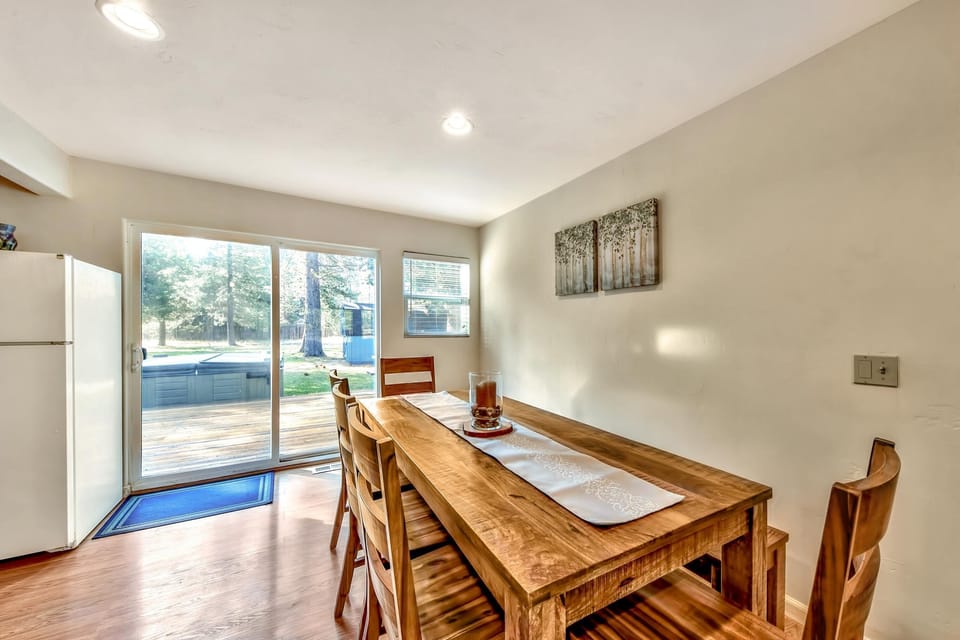Sunlight filters through sliding glass doors onto a solid wood dining table with matching chairs and a candle centerpiece.