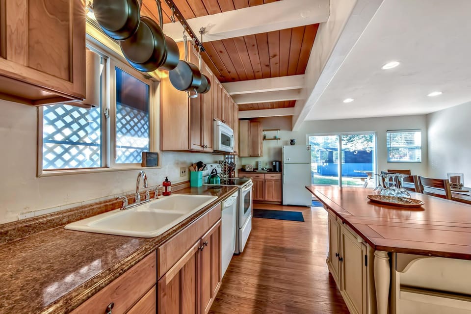 Kitchen with granite countertops, wooden cabinets, double sink, and an island extending into the dining area.
