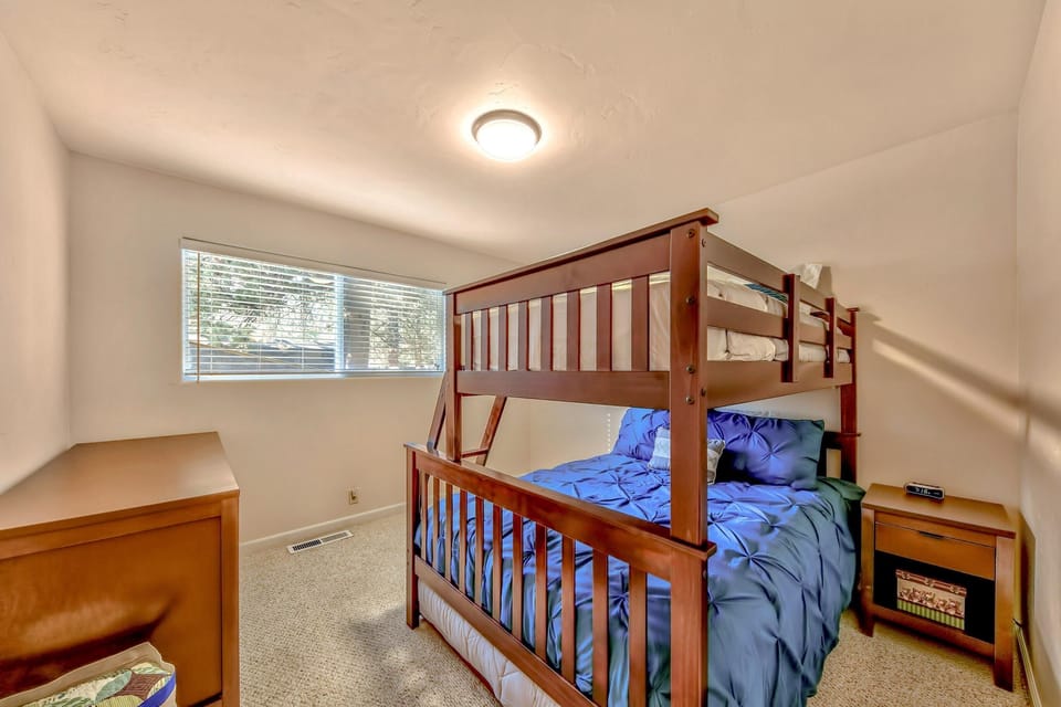 Wall-length window with white blinds fills the bedroom with natural light, highlighting the wood bunk bed and matching furniture.
