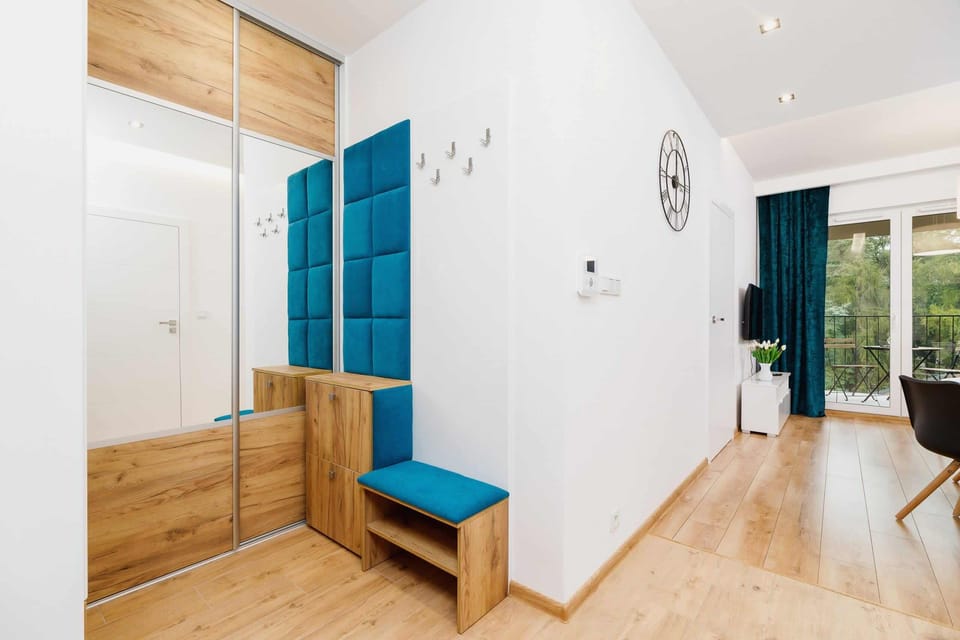 A bright hallway with a small bench, a coat rack, and a clock on the wall. The wooden flooring continues throughout.