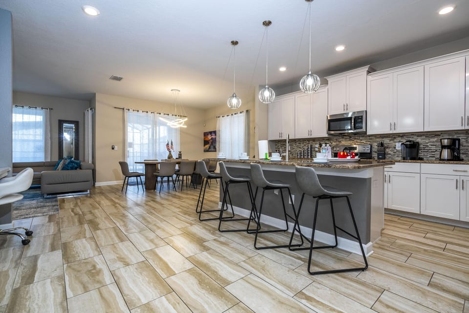 Granite-topped kitchen island with four gray bar stools under metal cage pendant lights and tiled flooring.