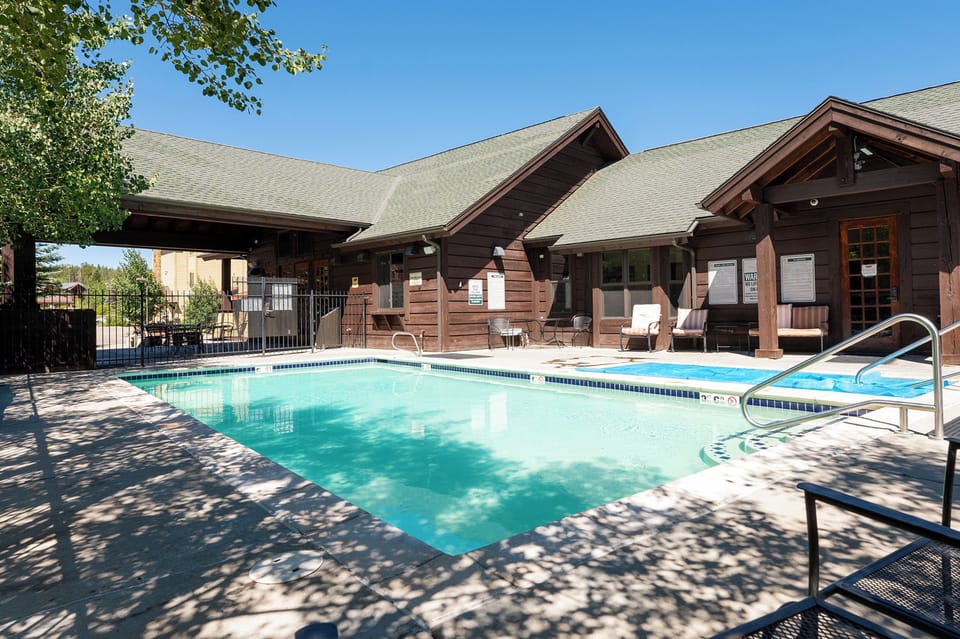 Charming wooden lodge building with outdoor swimming pool and seating area under clear blue skies.