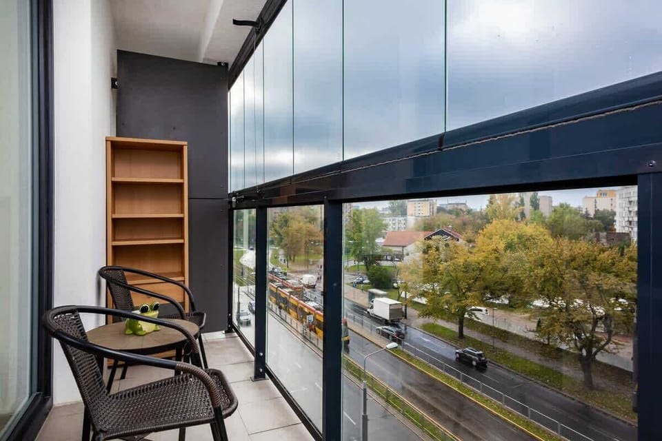 A stylish balcony with glass railings, wooden flooring, and a pair of chairs for enjoying the view outside.