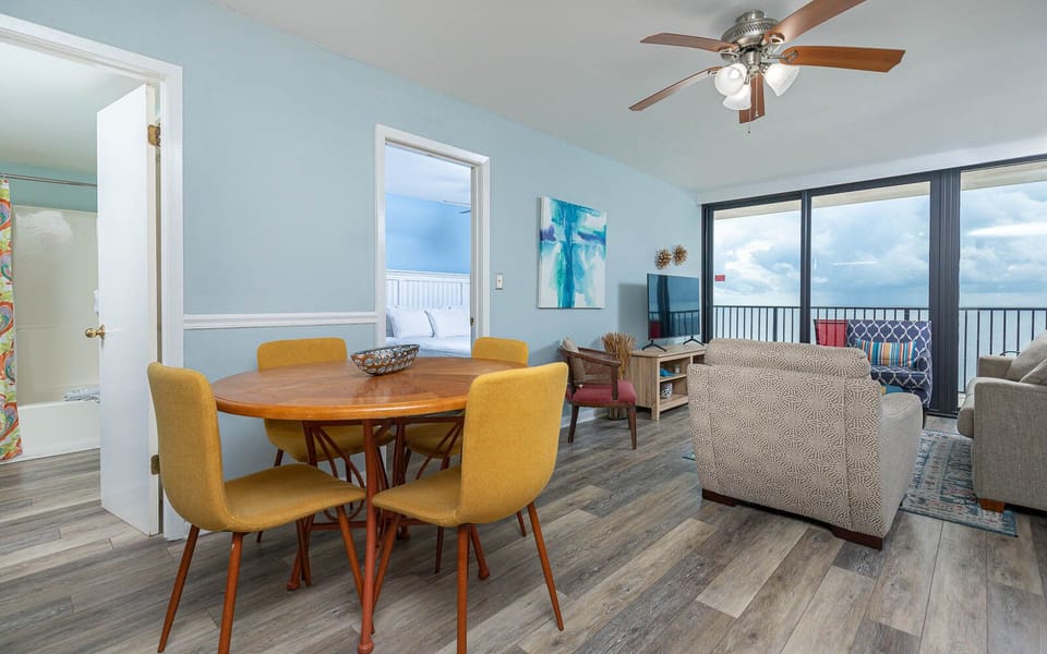 This cozy living area features a stylish round dining table, a TV, and a stunning beachfront view through large windows