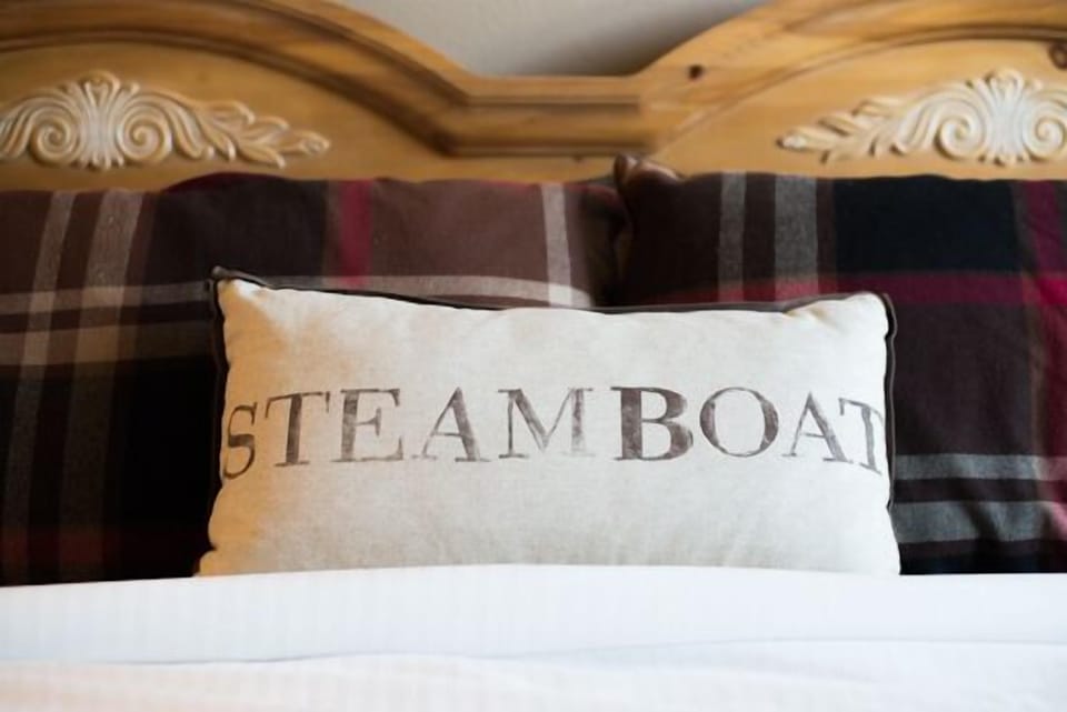 Settle into your cozy retreat with an ornate wooden headboard and charming plaid accents that create the perfect mountain lodge atmosphere.
