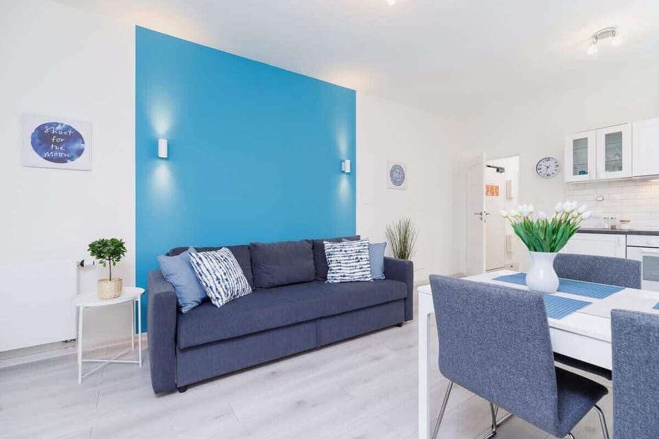 A living room with blue and white decor, including a sofa and accent wall. The room is open and connects seamlessly with the kitchen area.