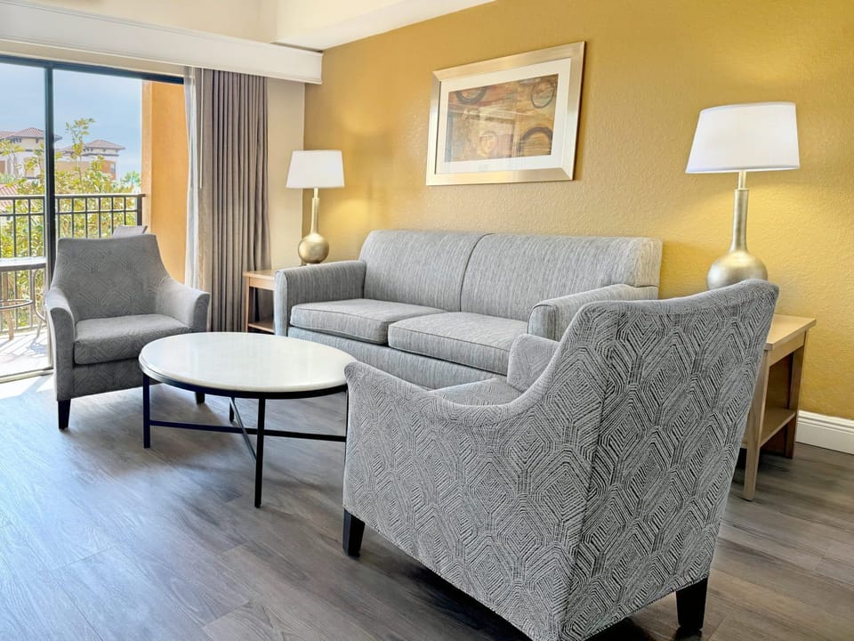 Living room with a grey sofa, two armchairs, and a coffee table — balcony visible through the window behind
