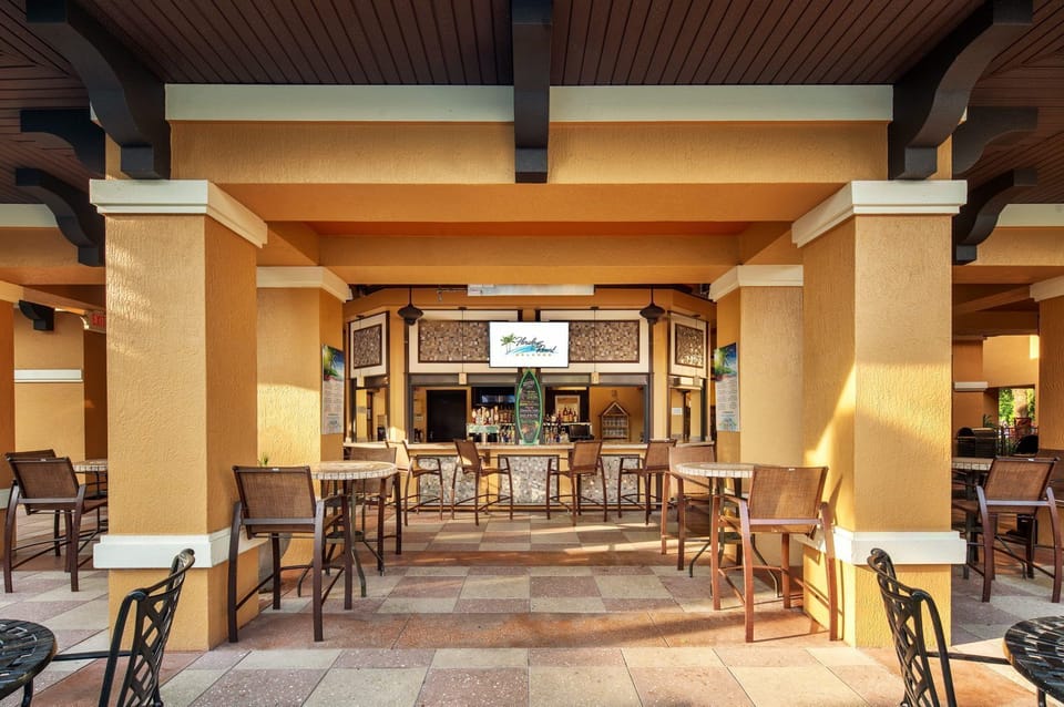 Stone-topped bar counter with tall stools and pendant lighting at the poolside bar and grill