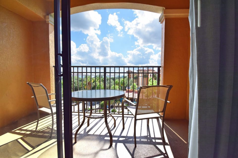 Round table and two chairs on the private balcony, overlooking green trees under a clear sky