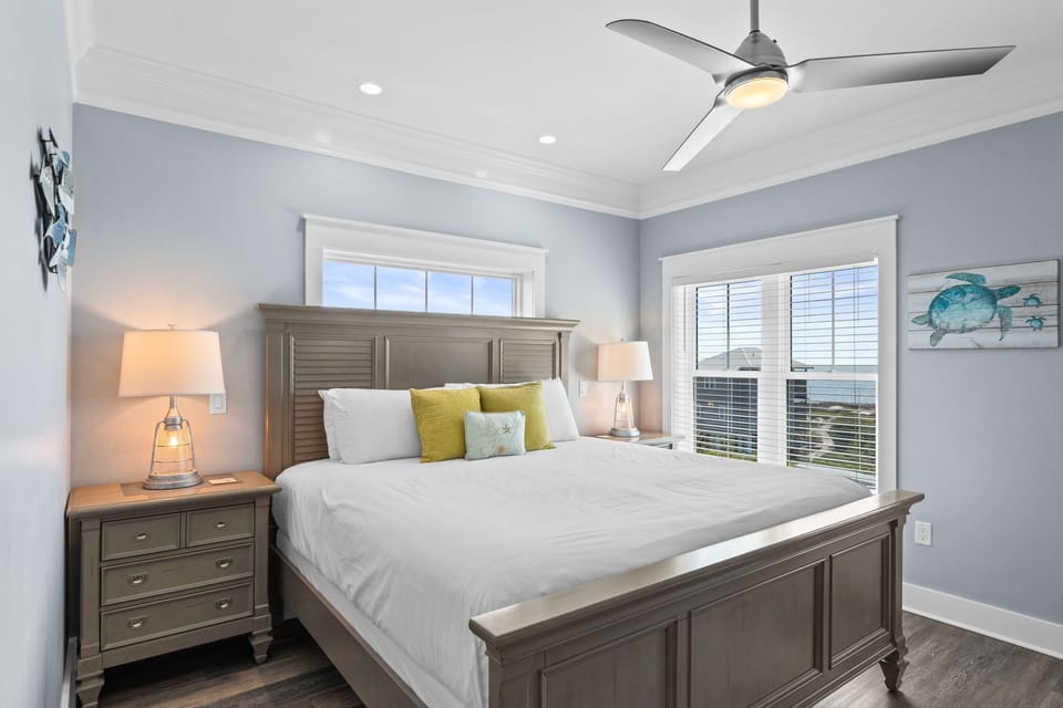 Rest peacefully in your coastal-inspired bedroom with crisp linens, gentle ceiling fan, and ocean artwork creating the perfect seaside retreat.