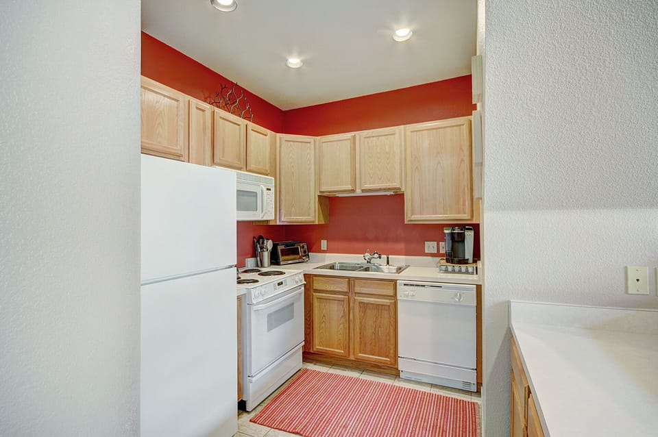 A small kitchen with light wood cabinets, white appliances including a refrigerator, stove, microwave, and dishwasher.
