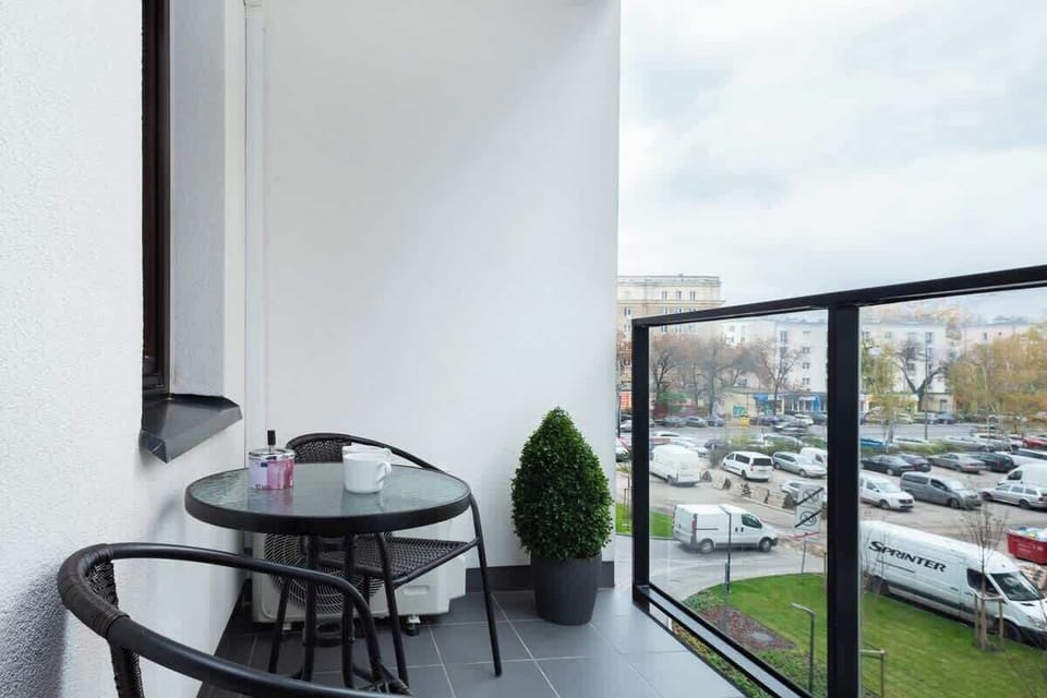 A balcony with chairs and a small table, overlooking a busy cityscape and providing an outdoor relaxation space.