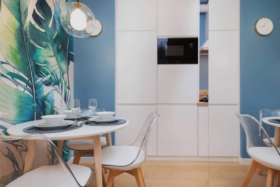 A cozy dining area with a small table and chairs, decorated with tropical-themed wallpaper featuring green leaves.