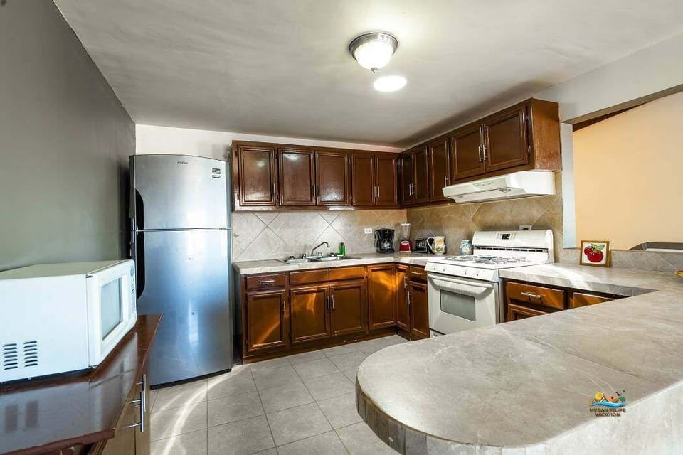 This kitchen features expansive counter space, custom wood cabinets, large sinks, a modern dishwasher, plus a coffee maker, toaster, microwave, and refrigerator with icemaker . A breakfast bar connects to the ocean-view dining area