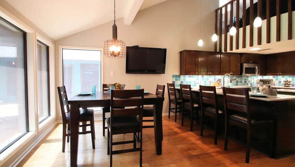 Dining room has bar-height chairs seating 8 around the table. Some chairs are at the sink counter bar, adding extra seating. With a 60" TV, this space doubles as a cozy gathering spot for meals, conversation, and entertainment.