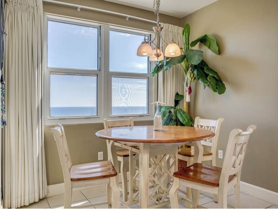 Your bright dining space offers ocean views while you enjoy meals together, with elegant pendant lighting and tropical plants creating an inviting atmosphere.