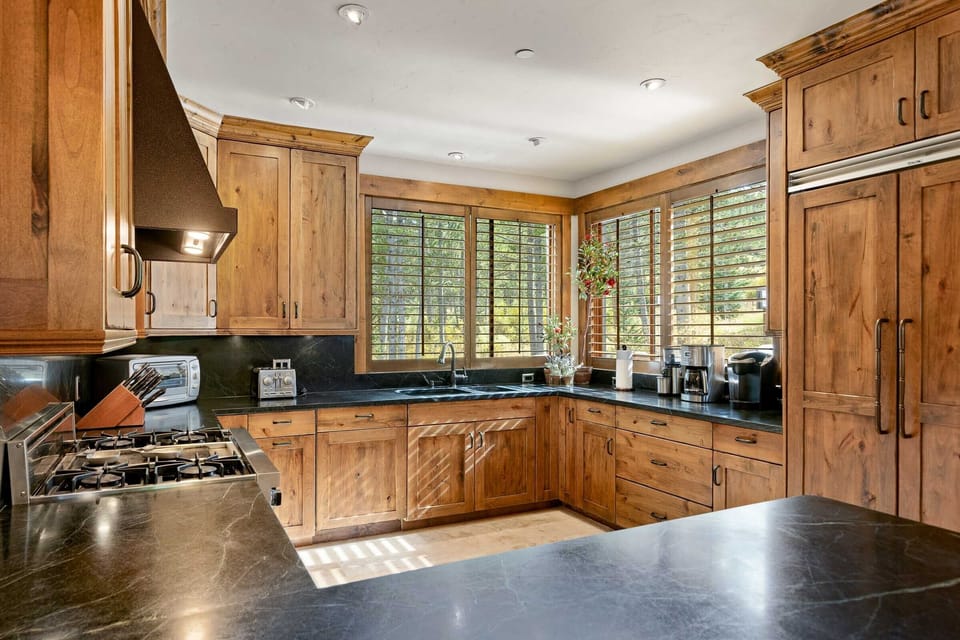 A kitchen with wooden cabinets, dark countertops, a stainless steel stove, and a window with ample natural light coming in.