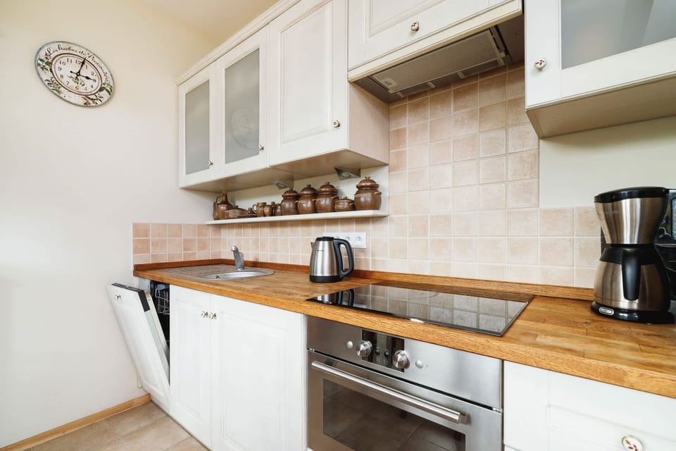 Close-up view of a kitchen with a sink, stove, and white tiled backsplash. Counter space includes modern appliances.