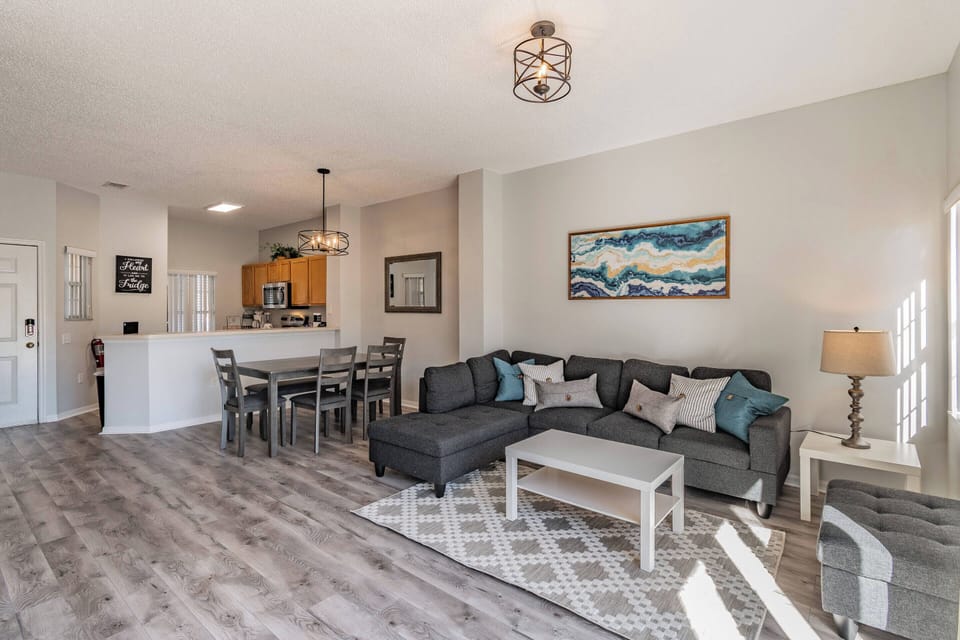 Experience a chic living area with soft gray sofas perfect for relaxation, highlighted by a modern light fixture. A vibrant artwork adds color, and the open layout effortlessly connects to the dining space, ideal for socializing.