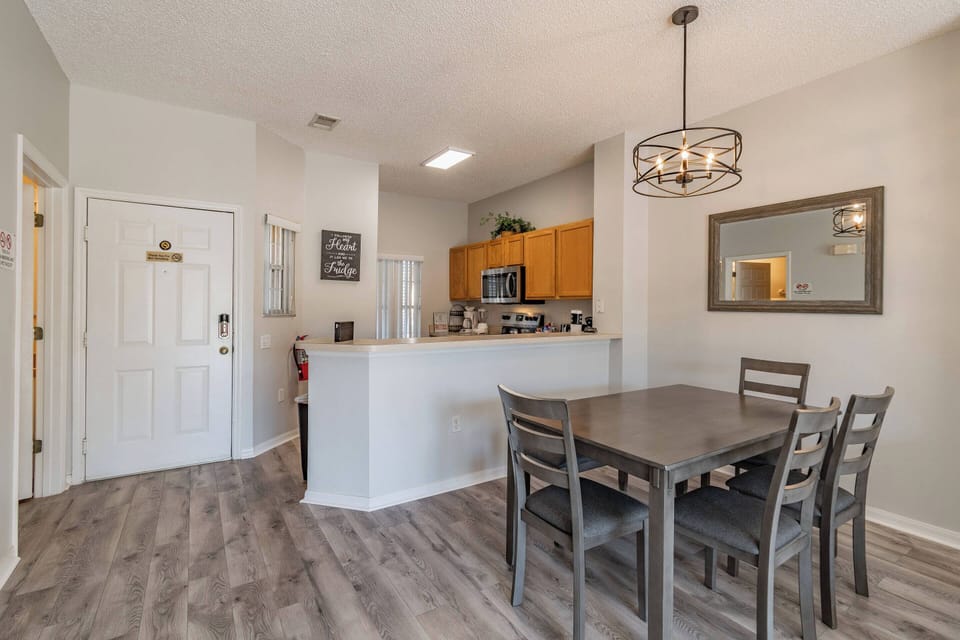 This bright dining area boasts a modern wooden table with stylish gray chairs, ideal for shared meals. The contemporary light fixtures and sleek cabinetry enhance the space, while the open layout ensures a light and airy feel.