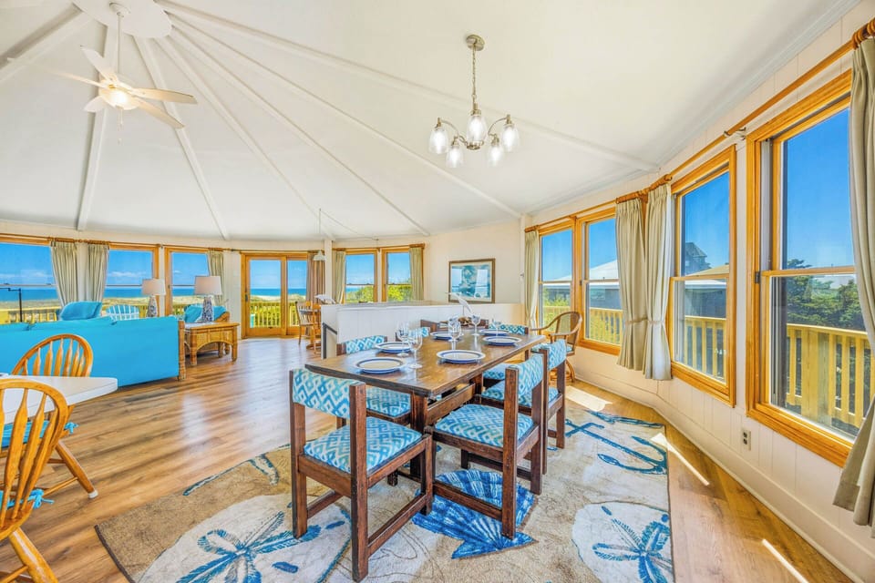A bright, airy dining room and open-plan living area frames stunning ocean views through walls of golden-trimmed windows, inviting you to savor meals and relaxed moments surrounded by sea breezes and natural sunlight.