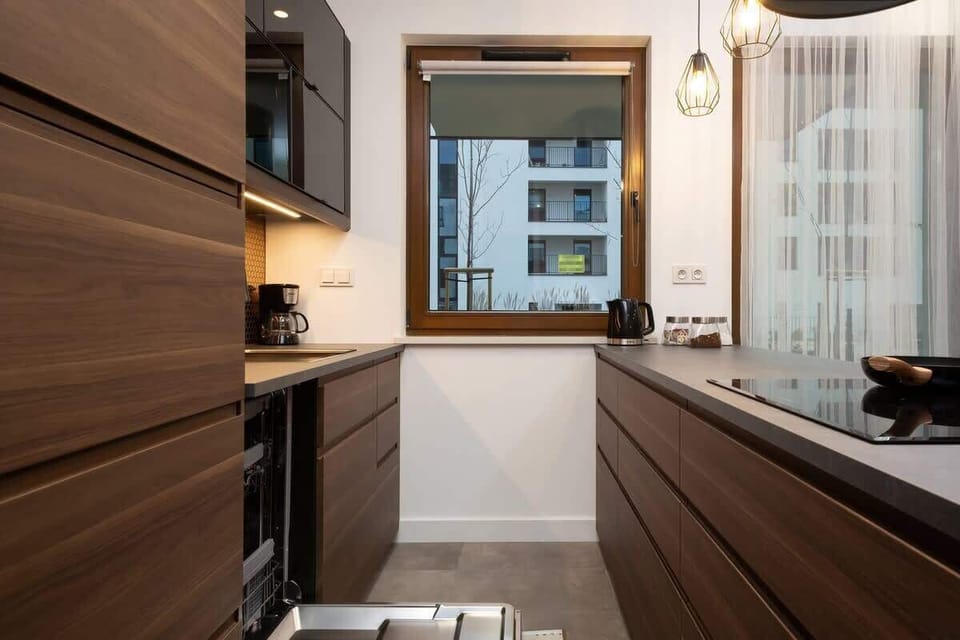 A compact but functional kitchen with wooden cabinets, a built-in oven, and a view of the outside through a large window.