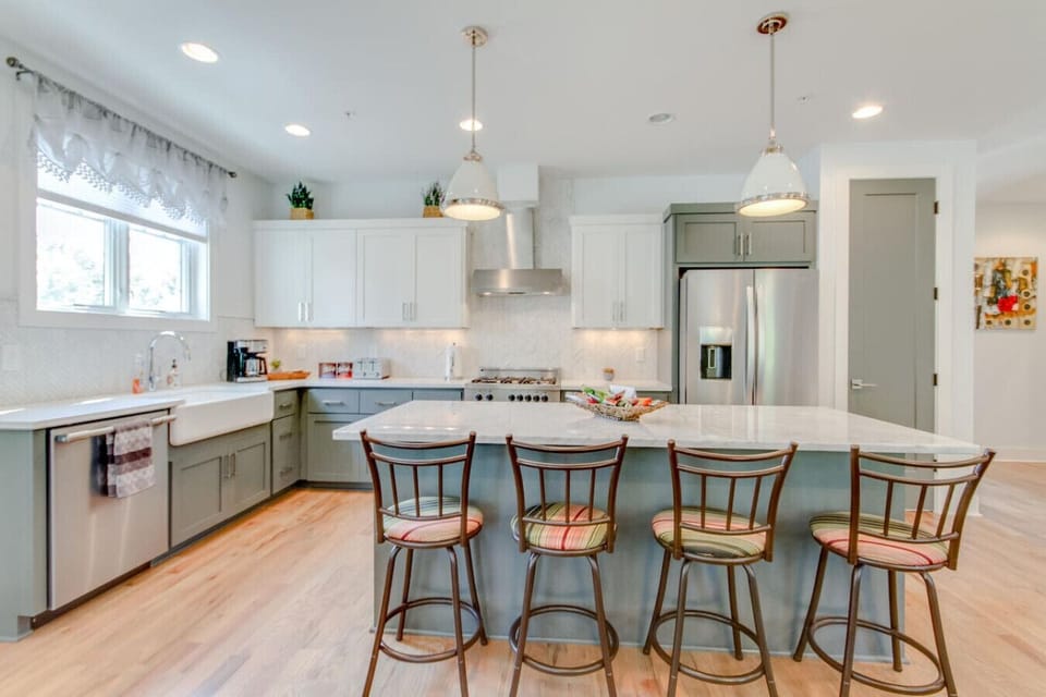 Kitchen with gray-green cabinets, a white island with bar stools, pendant lights, and stainless steel appliances