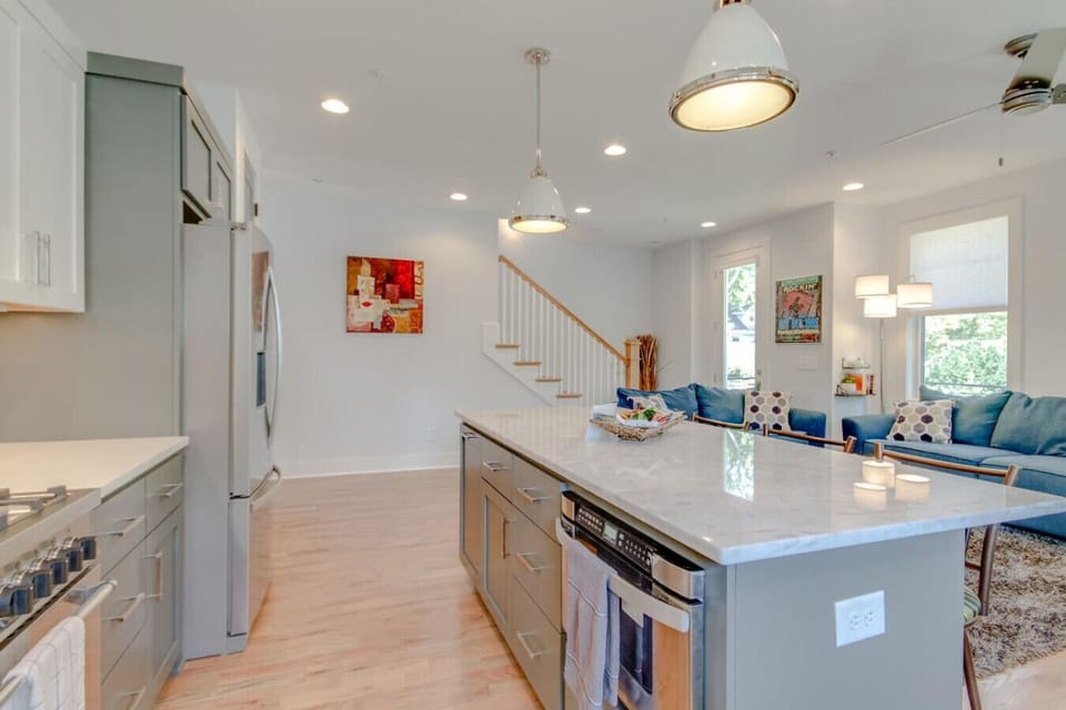 Kitchen showing the island, stainless steel refrigerator, pendant lights, and staircase