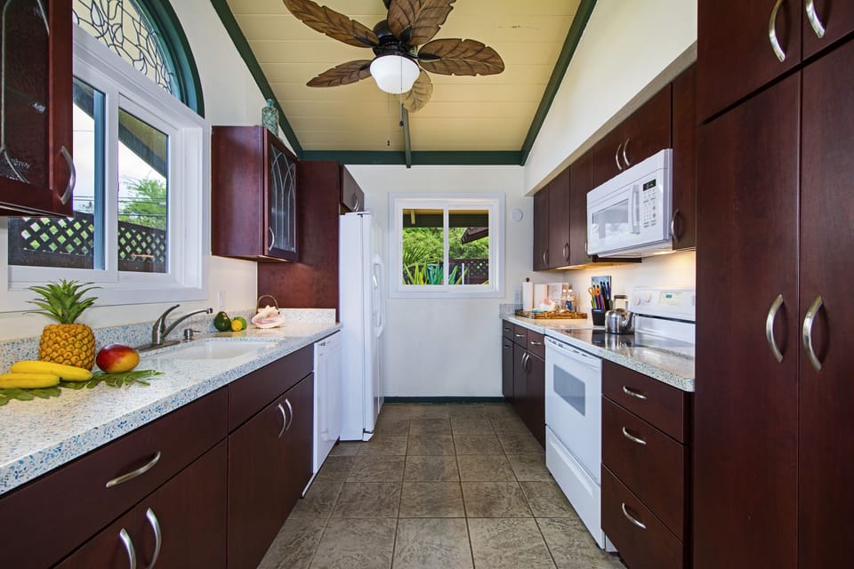 Bright and airy kitchen with rich wood cabinetry, ceiling fan, and window views for a comfortable cooking space.