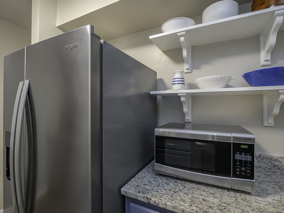 Microwave, side by side French door refrigerator, and open shelving modernize this updated kitchen