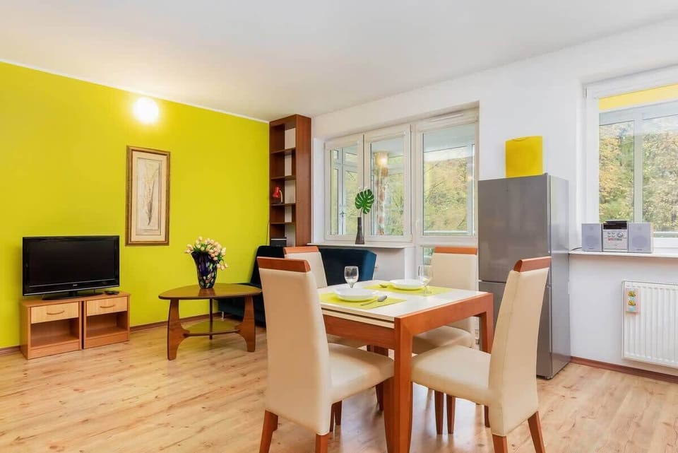 A dining space within the living room, with a table and chairs, and a yellow accent wall adding warmth.